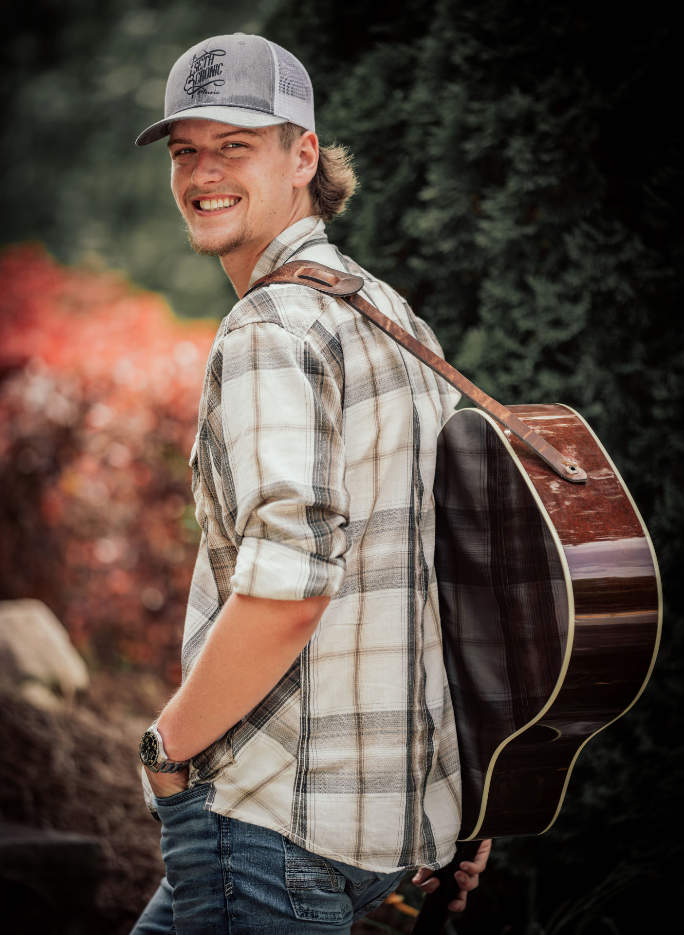 Seth Cronic smiling outdoors with his guitar case and Seth Cronic Music hat
