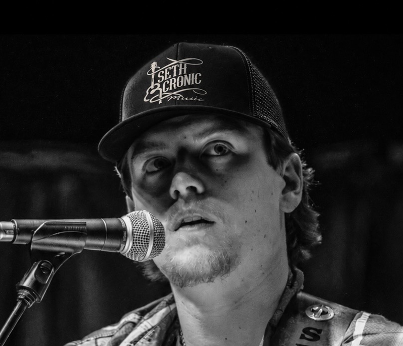 Seth Cronic at the microphone wearing a Seth Cronic Music cap